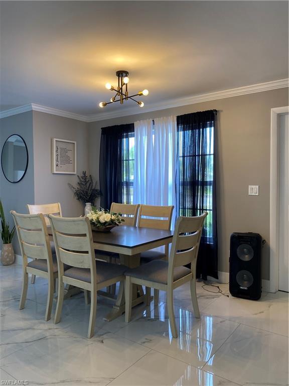 Image 2: Dining space with ornamental molding, a chandelier, and light marble finish flooring