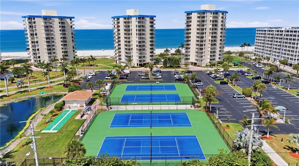 Image 3: Community amenities featuring multiple tennis courts, a shuffleboard court, and a reflective pond - Virtually Edited Image