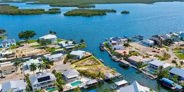 Image 4: Waterfront property featuring direct canal access, an undeveloped lot, and surrounding residential structures - Virtually Edited Image
