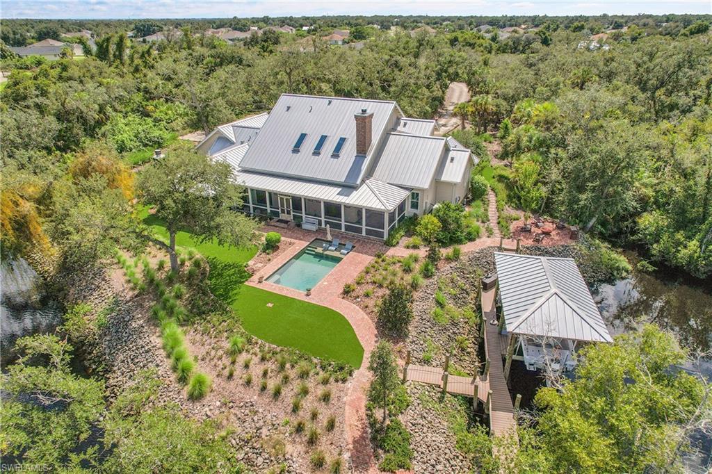 Image 2: Rear of the home showcasing a resort-style pool, lush synthetic lawn, and private dock, all surrounded by natural landscaping for exceptional privacy
