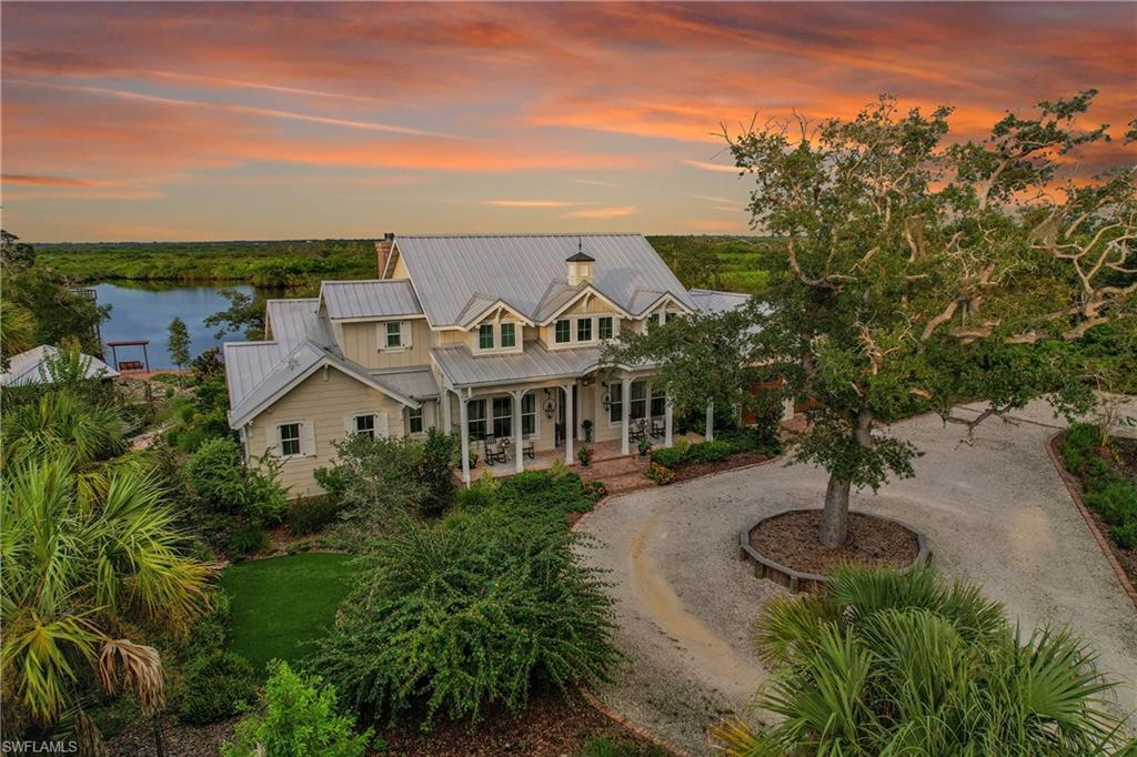 Image 3: Front elevation showing the home's welcoming porch, circular drive, landscaping with mature oak trees, with preserve and water views beyond