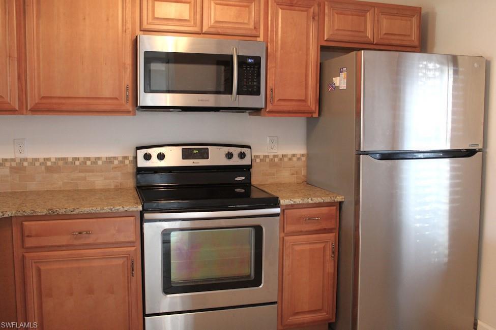 Image 4: Kitchen with appliances with stainless steel finishes, light stone countertops, and brown cabinets