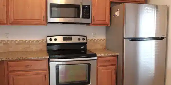 Image 4: Kitchen with appliances with stainless steel finishes, light stone countertops, and brown cabinets