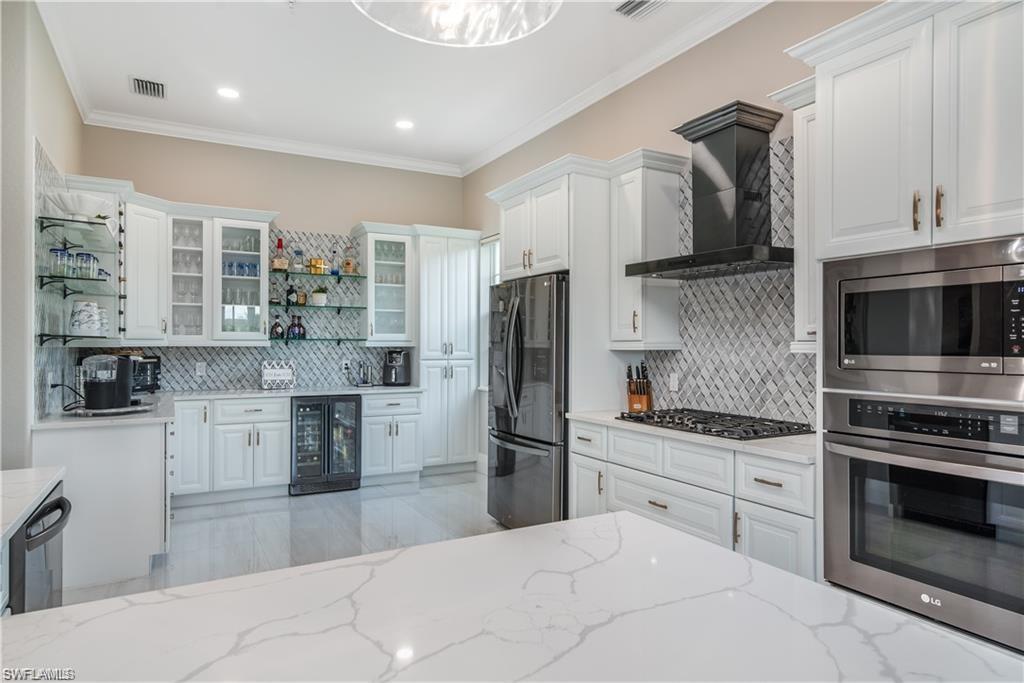 Image 1: Kitchen featuring white cabinetry, stainless steel appliances, open shelves, glass insert cabinets, and wall chimney range hood