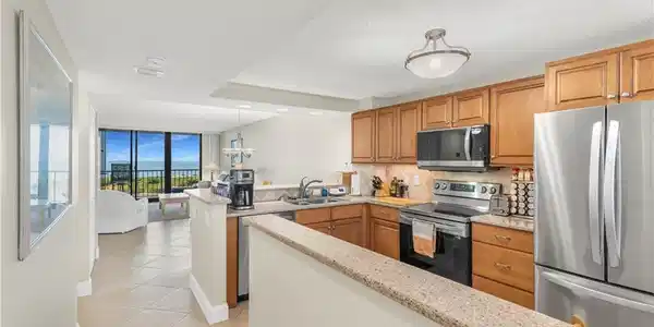 Image 2: Kitchen with stainless steel appliances, a peninsula, wood finish cabinetry, light tile patterned flooring, and hanging light fixtures