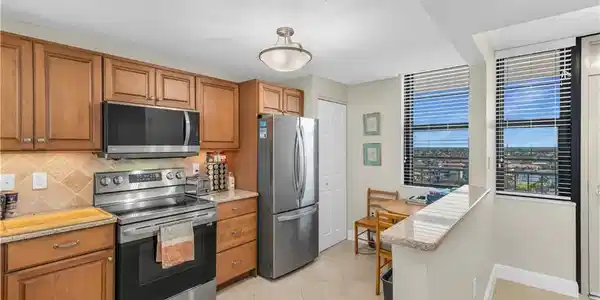 Image 3: Kitchen with stainless steel appliances, wood finish cabinets, light stone counters, a textured ceiling, and light tile patterned floors