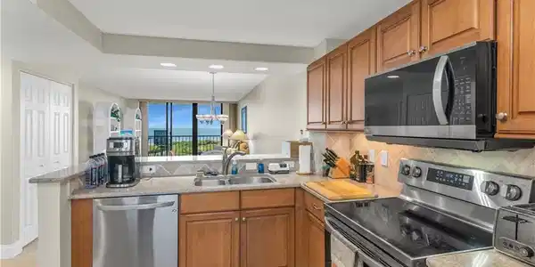 Image 4: Kitchen featuring stainless steel appliances, wood finish cabinetry, a peninsula, and light stone countertops