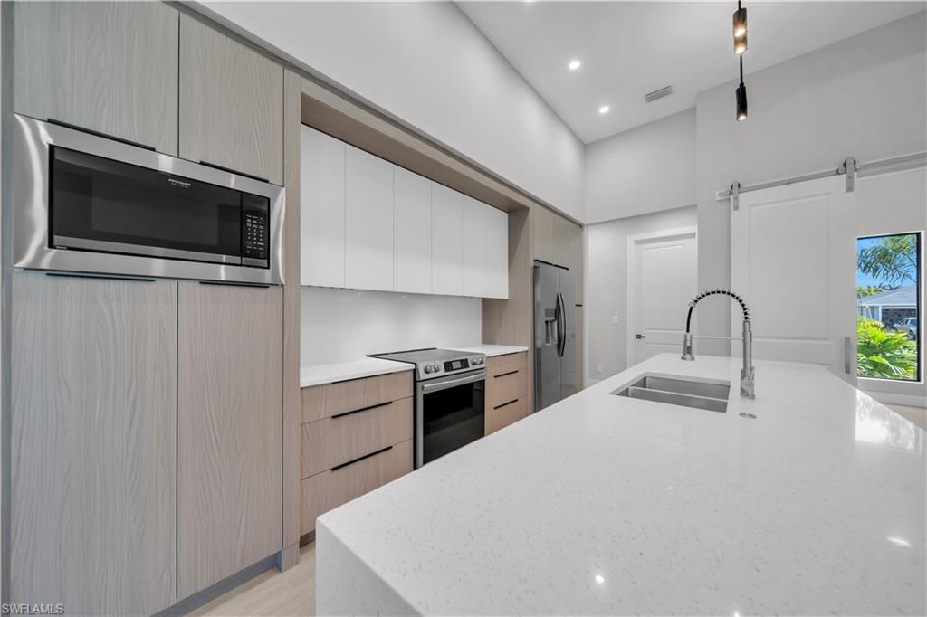 Image 4: Two tone kitchen featuring modern cabinets, two tone cabinetry, light stone counters, stainless steel appliances, and a barn door
