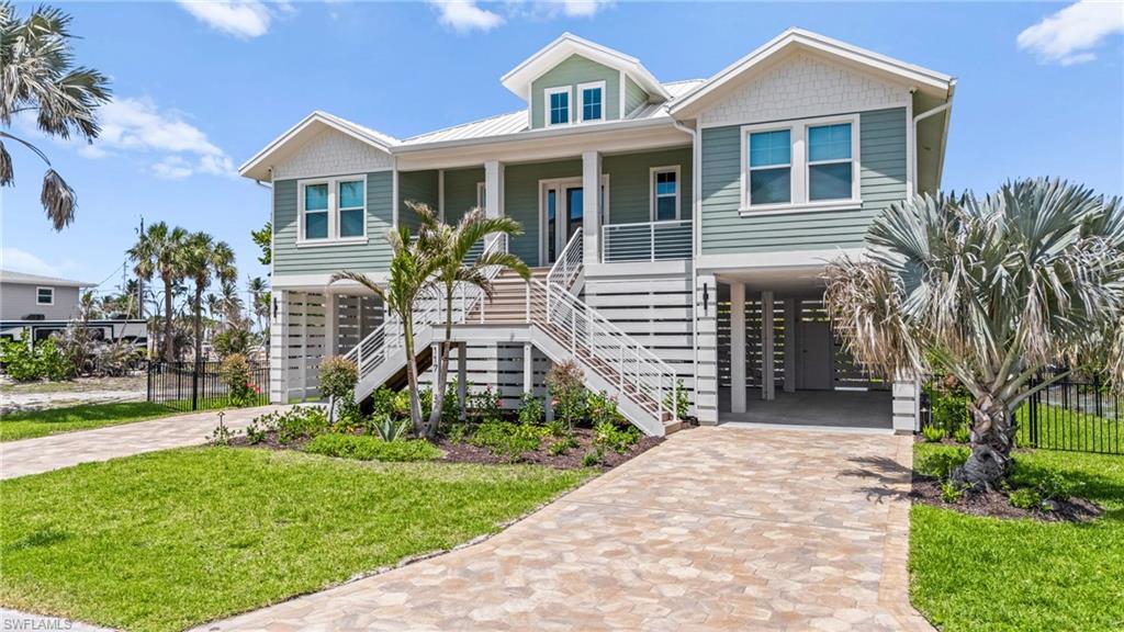 Image 2: Coastal inspired home with stairway, driveway, a carport, covered porch, and a front yard. virtually edited photo