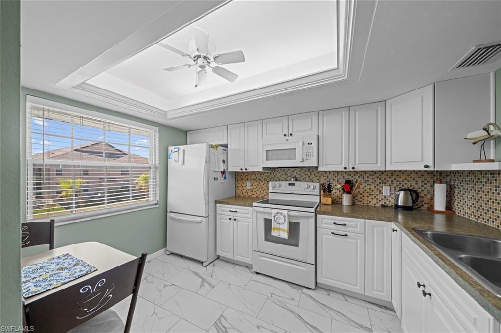 Image 4: Kitchen featuring white cabinetry, a mosaic tile backsplash, solid surface countertops, white appliances, and large format floor tiling