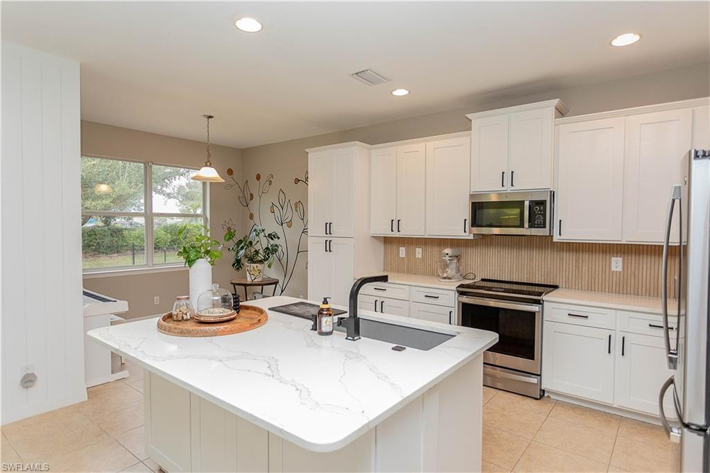 Image 2: Kitchen with stainless steel appliances, white cabinets, and light stone counters