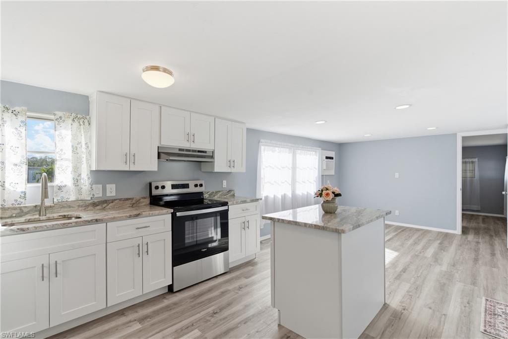Image 2: Kitchen with stainless steel electric range oven, white cabinetry, a kitchen island, and healthy amount of natural light