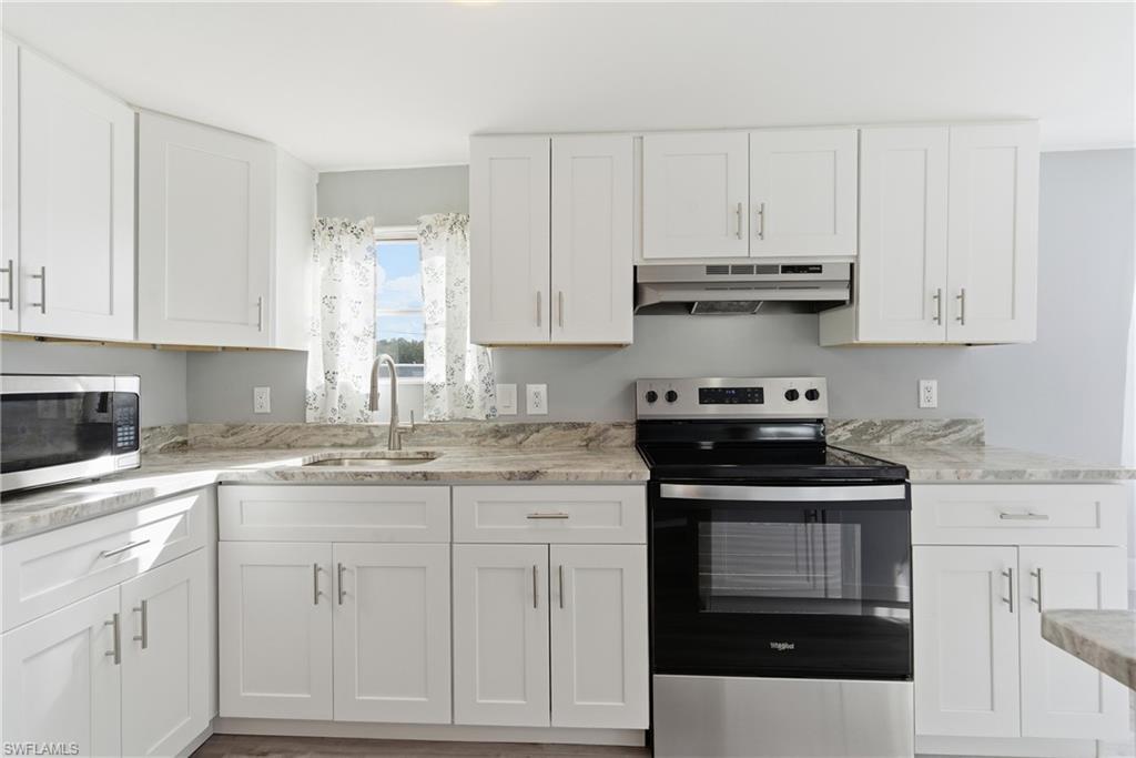 Image 3: Kitchen with stainless steel appliances, white cabinets, under cabinet range hood, and light stone countertops