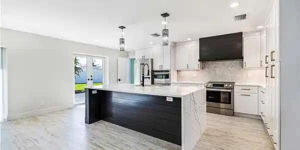 Image 2: This kitchen is a show stopper! Contemporary kitchen featuring a waterfall island with quartz countertop, white shaker cabinetry, stainless steel appliances, and a custom made range hood