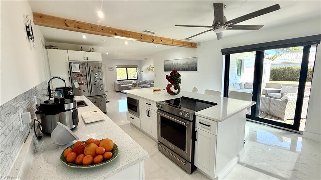 Image 3: Kitchen with white cabinets, stainless steel appliances, a center island, open floor plan, and light stone countertops