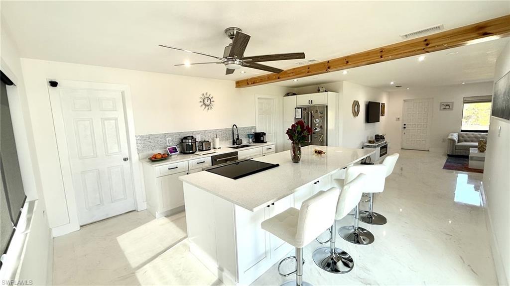 Image 4: Kitchen featuring white cabinetry, black appliances, a kitchen bar, a kitchen island, and tasteful backsplash