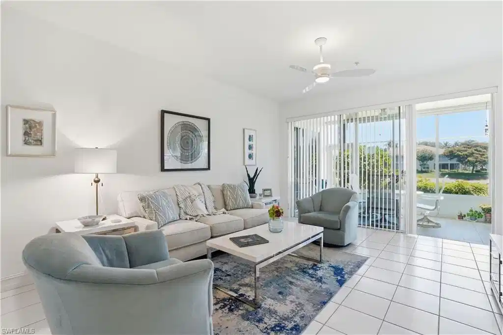 Image 1: Bright living space with white tile flooring and a patio featuring a white railing, accessible via a large glass sliding door with vertical blinds