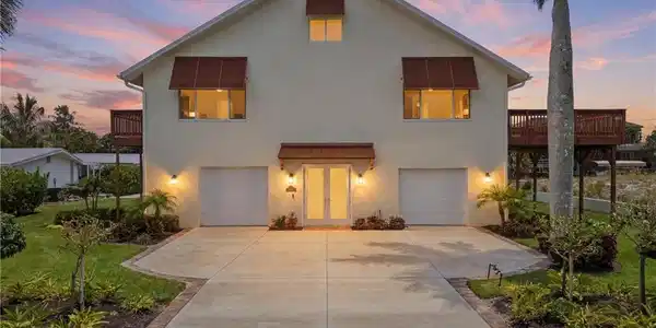 Image 2: Two-story stucco home featuring a central entry with transom window, two integrated garages, and two elevated wood decks