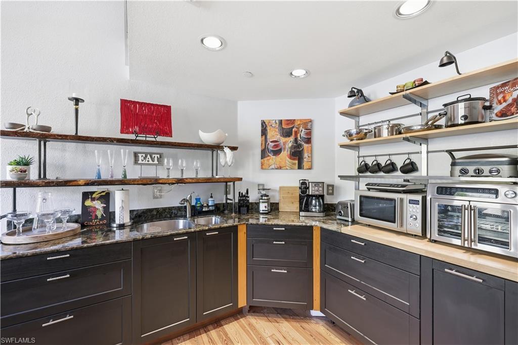 Image 3: Kitchen with open shelves, light wood-style flooring, dark stone countertops, recessed lighting, and stainless steel microwave