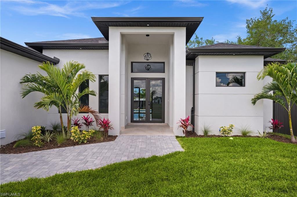 Image 1: Modern architectural facade featuring a prominent entryway, double glass panel doors, and a paver walkway