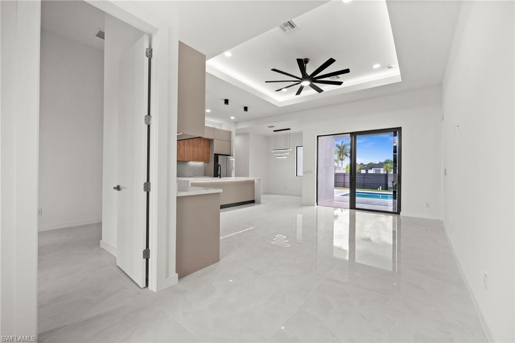 Image 3: Spacious interior featuring large format tile flooring, a modern kitchen with two-tone cabinetry and an island, a tray ceiling with recessed lighting and a ceiling fan, and sliding glass doors opening to an outdoor area with a swimming pool