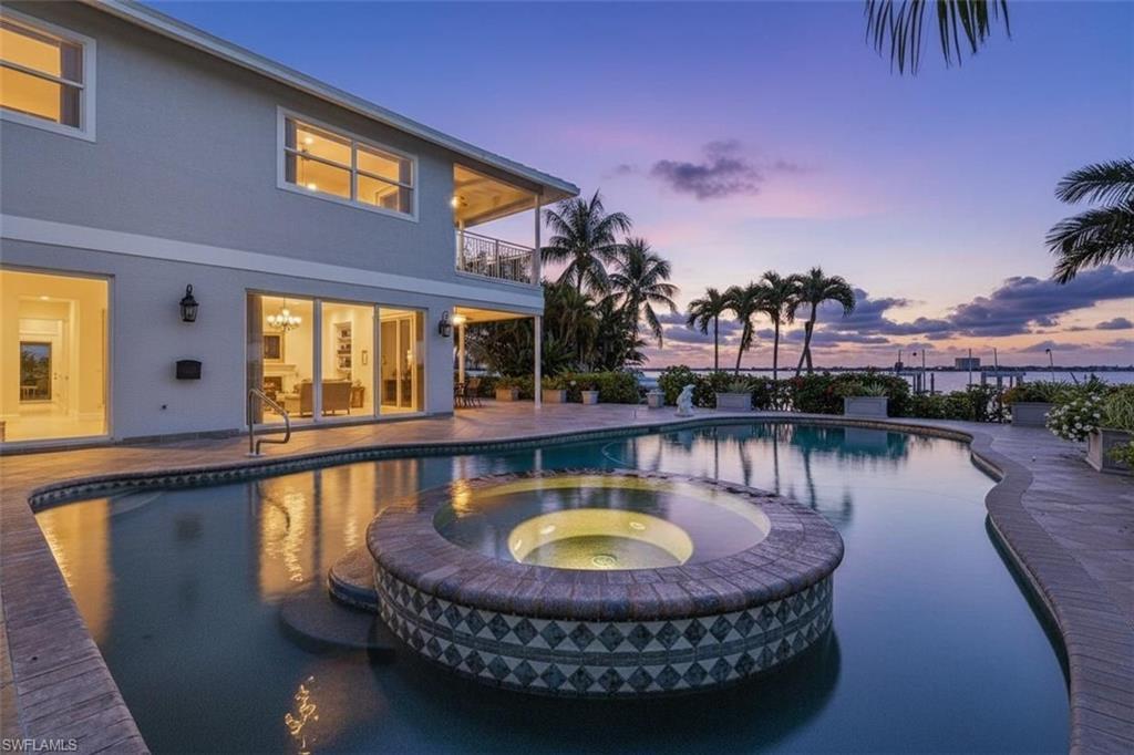 Image 2: Pool at dusk featuring a balcony, a patio, and a pool with connected hot tub