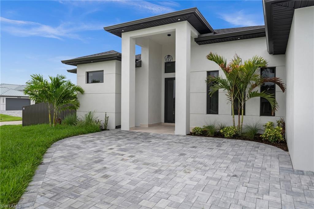 Image 3: Contemporary stucco exterior featuring a grand entryway, dark frame windows, a paver driveway, and mature palm trees