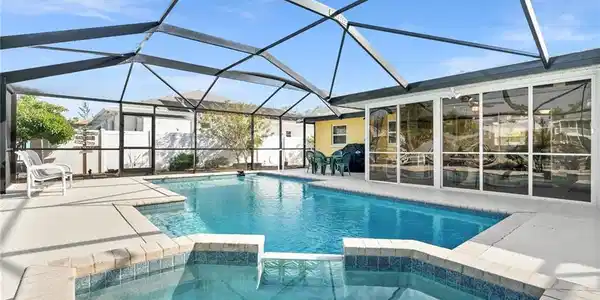 Image 3: View of swimming pool featuring a pool with connected hot tub, a sunroom, glass enclosure, and a patio area