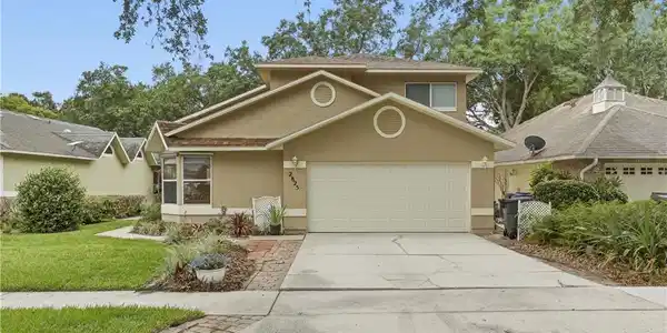 Image 4: Two-story stucco home featuring a two-car garage, concrete driveway, and front lawn with mature landscaping