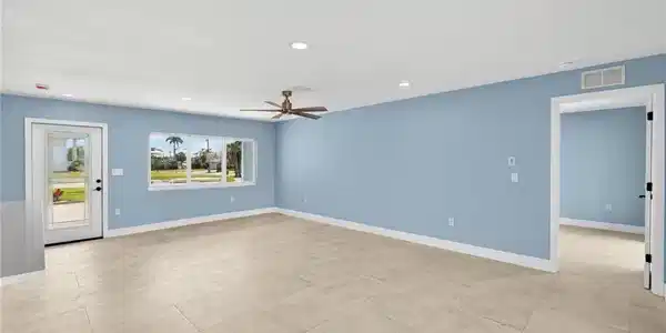 Image 3: Spacious interior with neutral tile flooring, recessed lighting, a modern ceiling fan, and a large window overlooking exterior landscaping