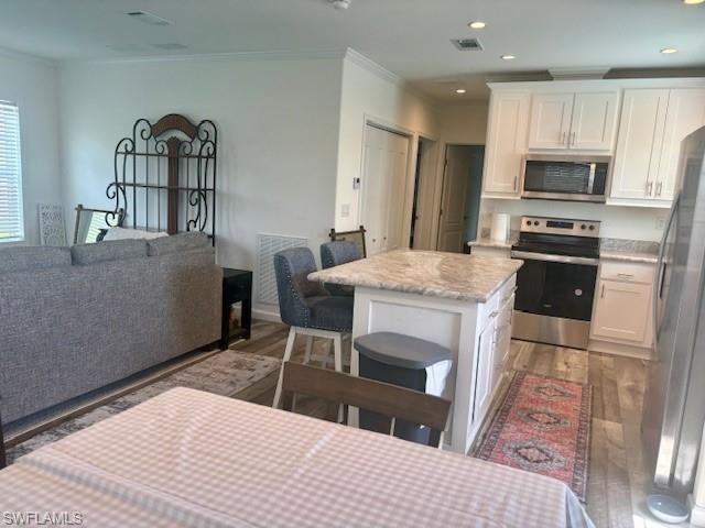 Image 3: Kitchen with open floor plan, appliances with stainless steel finishes, white cabinetry, a breakfast bar, and crown molding