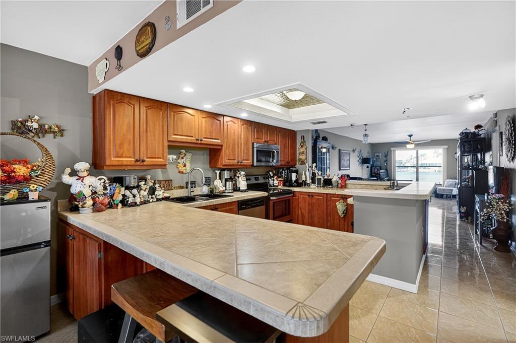 Image 2: Kitchen featuring a peninsula, wood finish cabinets, a kitchen bar, stainless steel appliances, and a tray ceiling