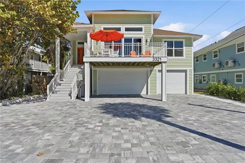 Image 1: Raised beach house featuring an attached garage, decorative driveway, and a balcony - Virtually Edited Image