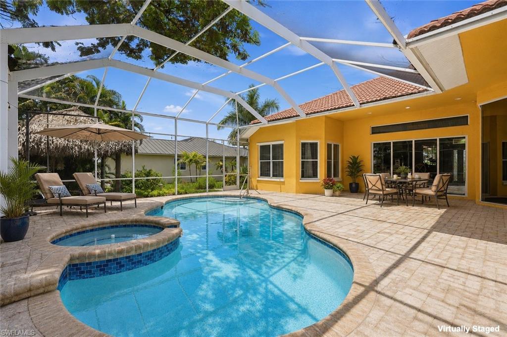 Image 2: Screened lanai featuring a free-form swimming pool with an integrated spa, paver decking, and a stucco exterior with a tile roof