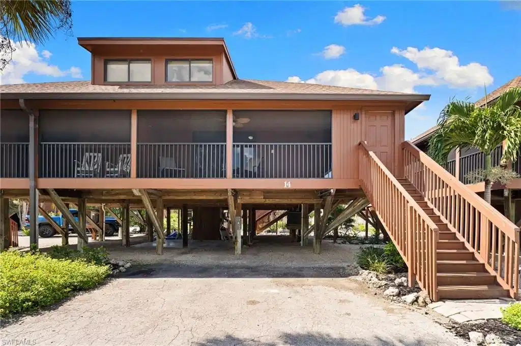 Image 1: Coastal home with a carport, dirt driveway, a shingled roof, a deck, and stairway