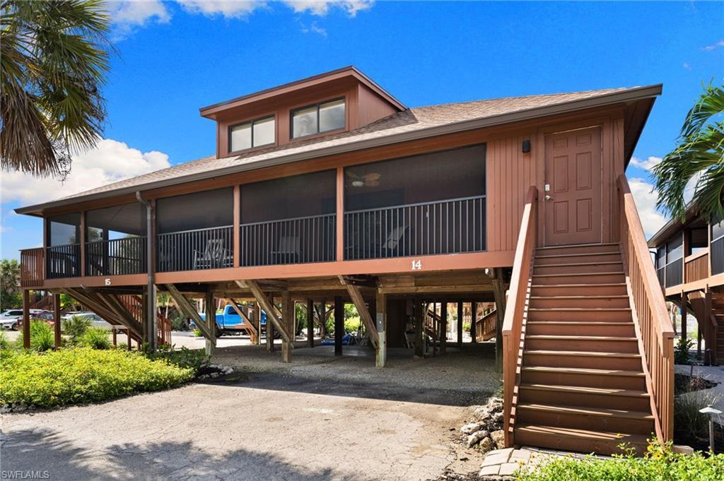 Image 2: View of front of house with dirt driveway, stairway, a carport, roof with shingles, and a sunroom