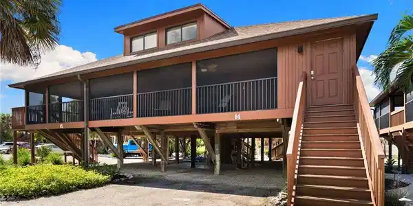 Image 2: View of front of house with dirt driveway, stairway, a carport, roof with shingles, and a sunroom