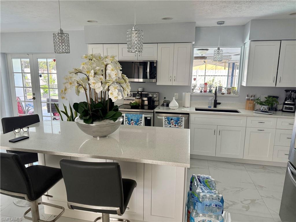 Image 3: Kitchen with white cabinetry, light stone counters, and stainless steel appliances