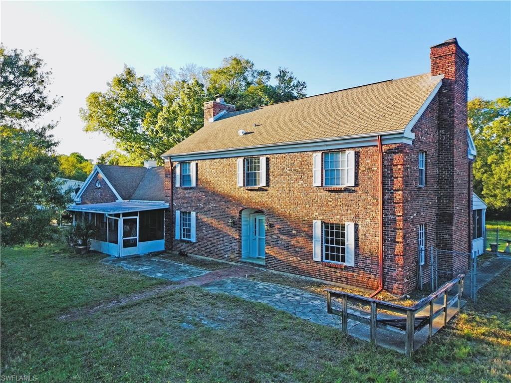 Image 1: Front of property featuring a chimney, brick siding, a sunroom, and a lawn