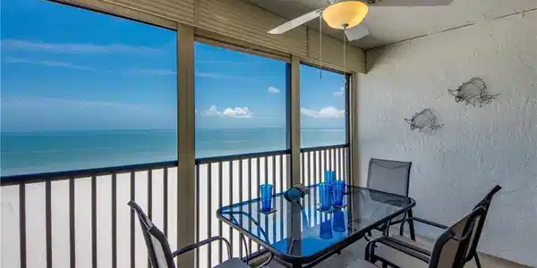 Image 2: Expansive balcony featuring a white textured wall, ceiling fan with integrated lighting, full-height windows, and a black railing overlooking the ocean