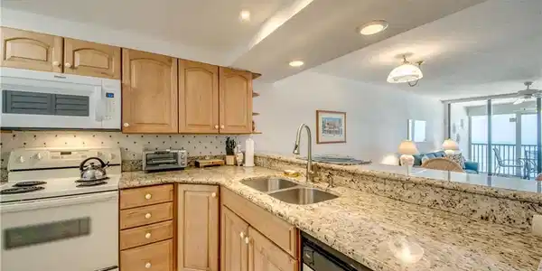 Image 4: Kitchen featuring light wood cabinetry, stone countertops, double basin sink with gooseneck faucet, and white appliances