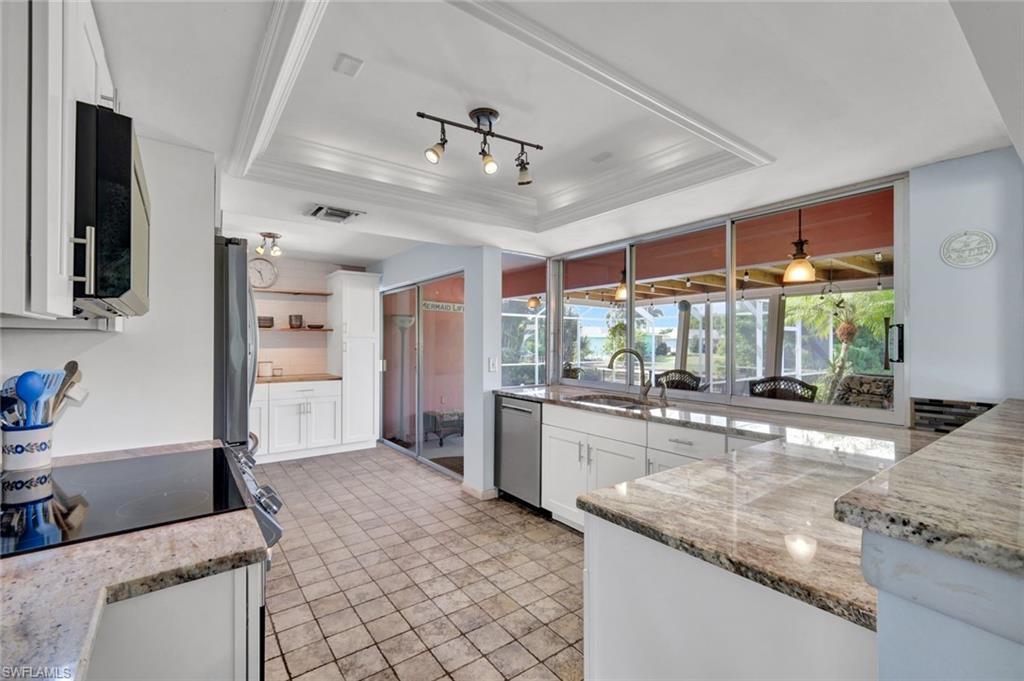 Image 4: Kitchen featuring stainless steel dishwasher, light stone countertops, a raised ceiling, plenty of natural light, and ornamental molding