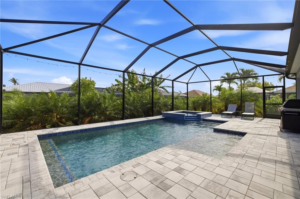 Image 1: Screened patio featuring a swimming pool with integrated spa, paver decking, and mature tropical landscaping