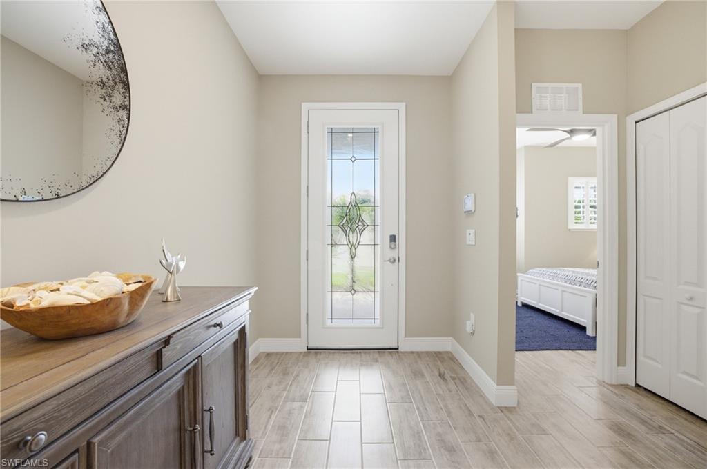 Image 3: Inviting entryway featuring wood-finish tile flooring, a white paneled door with decorative glass inserts, and a built-in storage cabinet with dark hardware