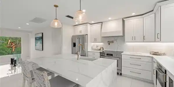 Image 4: Kitchen featuring light stone counters, hanging light fixtures, appliances with stainless steel finishes, an island with sink, and custom range hood