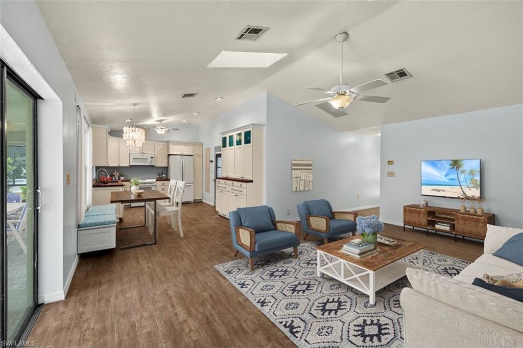 Image 4: Living room with hardwood / wood-style flooring, lofted ceiling, sink, and ceiling fan with notable chandelier