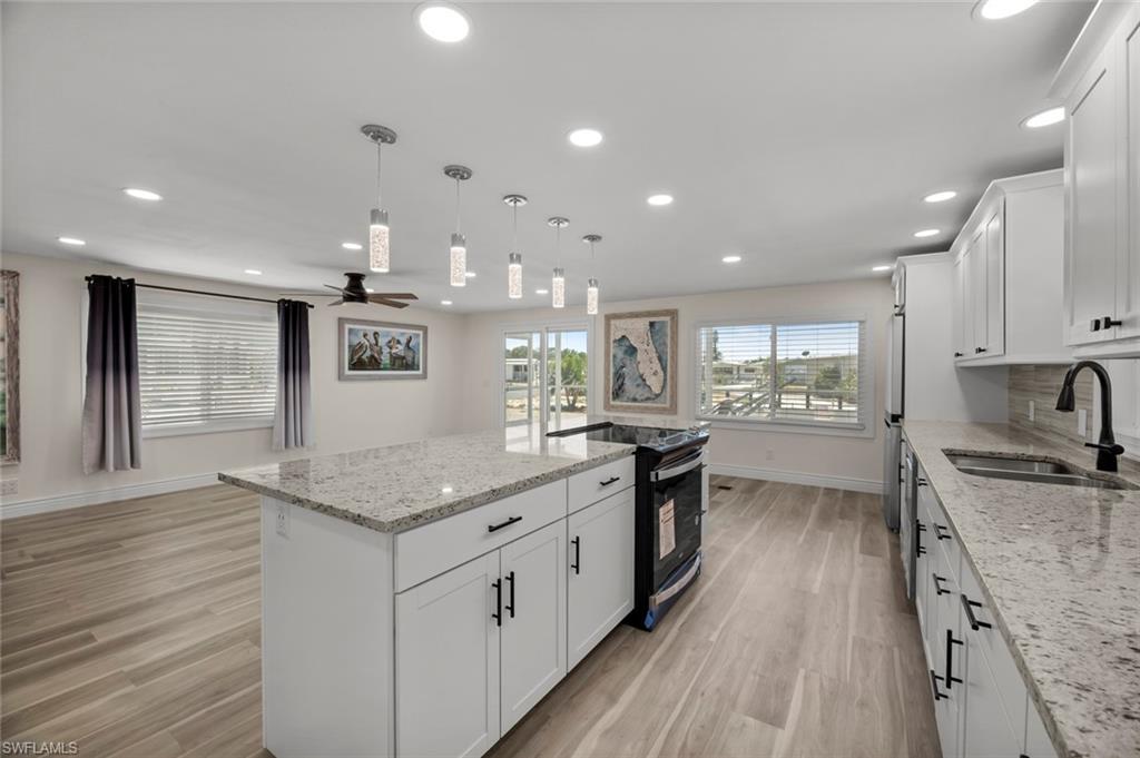 Image 4: Kitchen featuring white cabinetry, light stone countertops, decorative light fixtures, black electric range, and recessed lighting