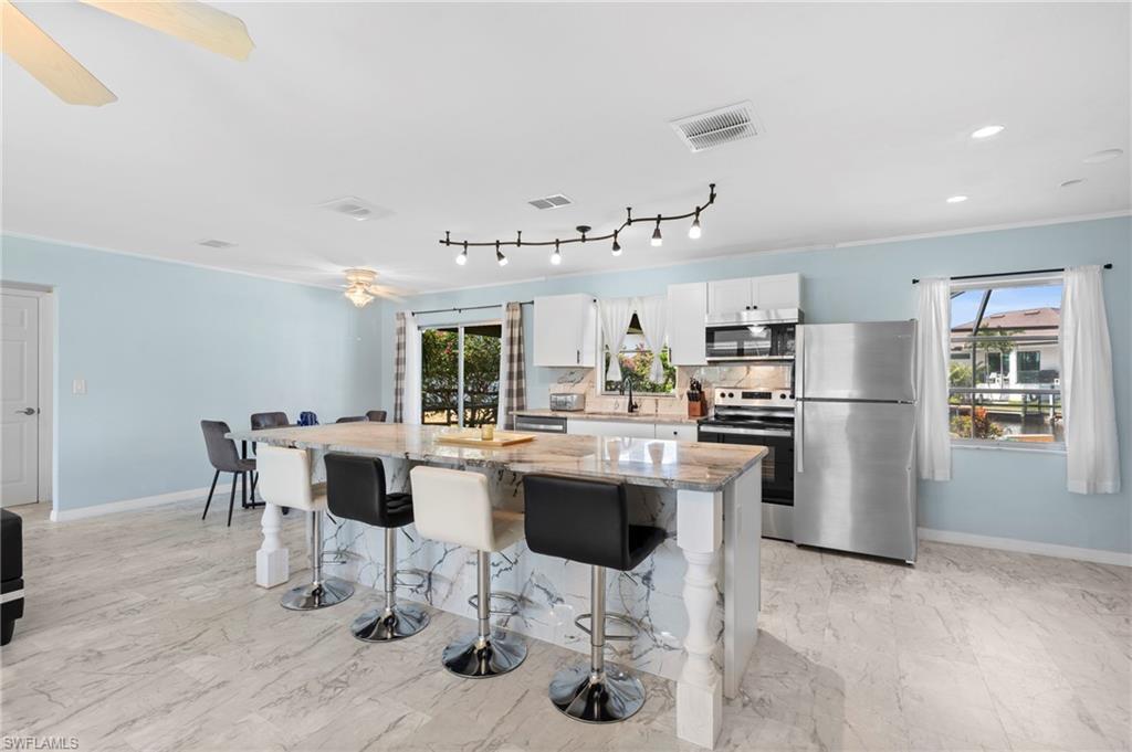 Image 3: Kitchen with appliances with stainless steel finishes, light stone countertops, a kitchen island, white cabinets, and a breakfast bar