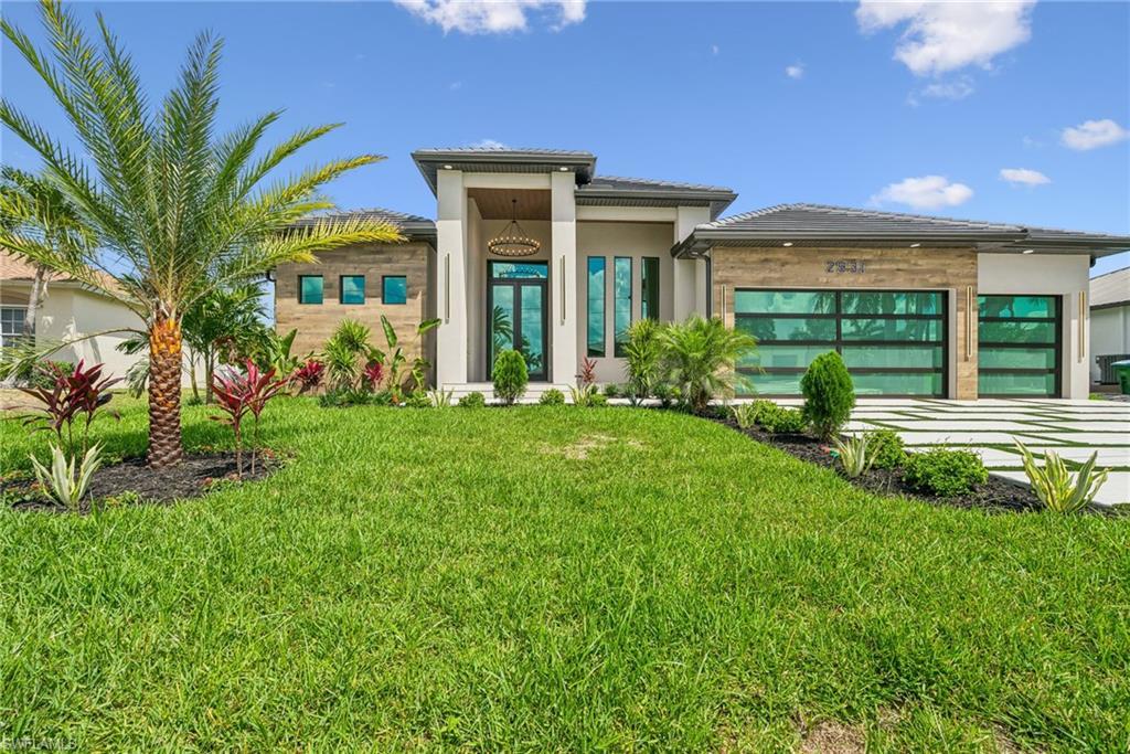 Image 2: Contemporary exterior featuring a lush green lawn, mature palm tree, modern landscaping, segmented driveway, and two glass-paneled garage doors