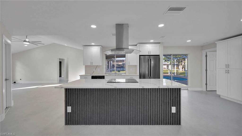Image 1: Kitchen featuring light stone counters, island range hood, high quality fridge, white cabinetry, and recessed lighting
